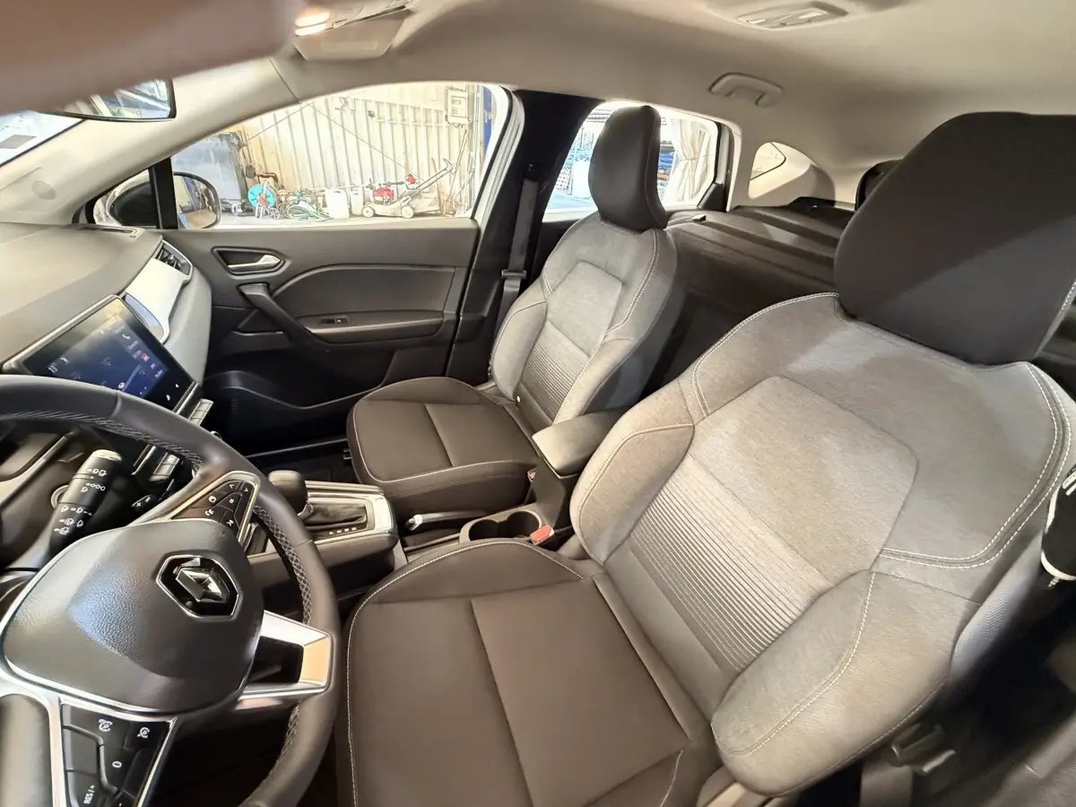 Vue intérieure côté conducteur du Renault Captur blanc 2021, avec sièges bicolores gris et noir et tableau de bord moderne.