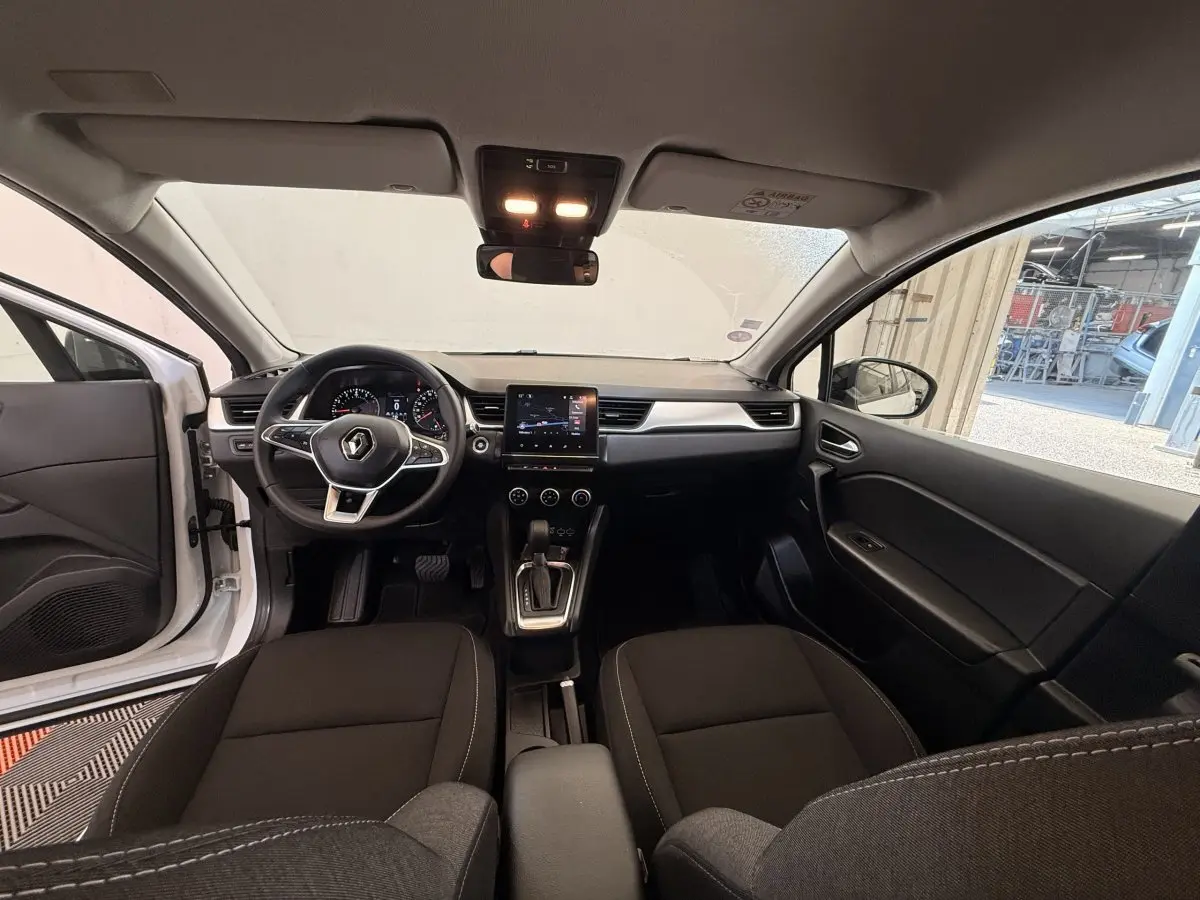 Vue intérieure avant du Renault Captur blanc 2021, montrant le tableau de bord avec écran tactile central et volant multifonctions.