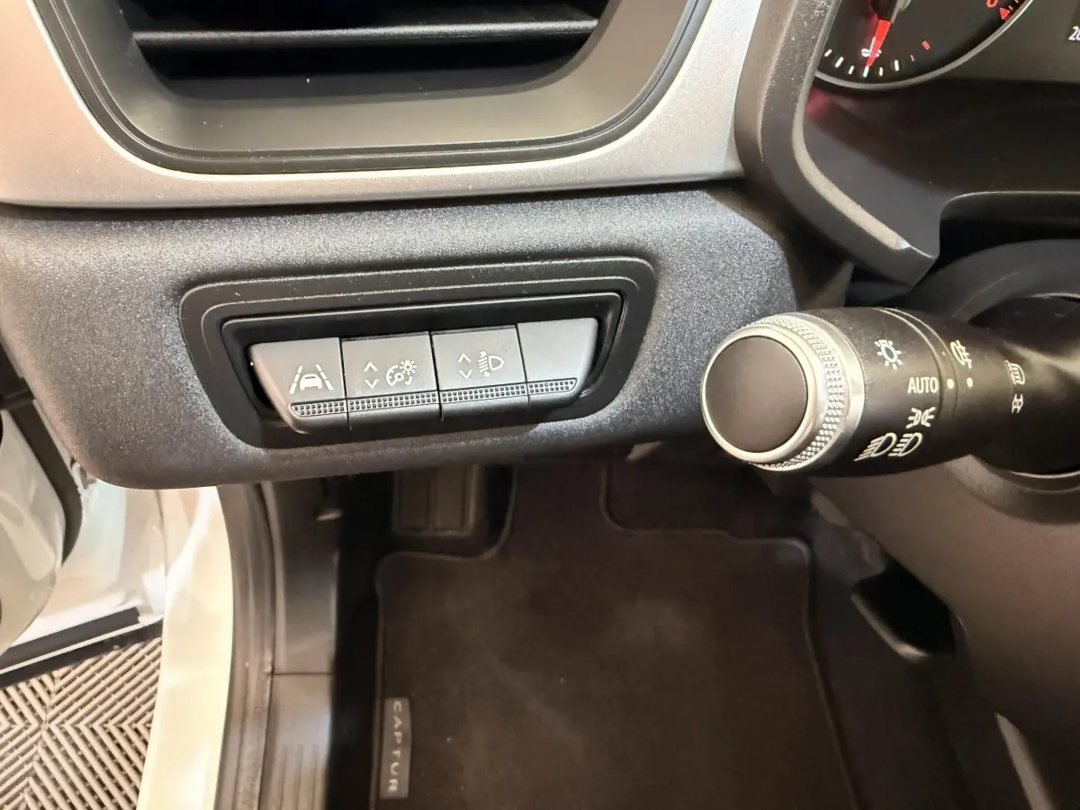 Vue intérieure côté gauche du tableau de bord du Renault Captur blanc, avec commandes d'assistance à la conduite et commodo des phares.