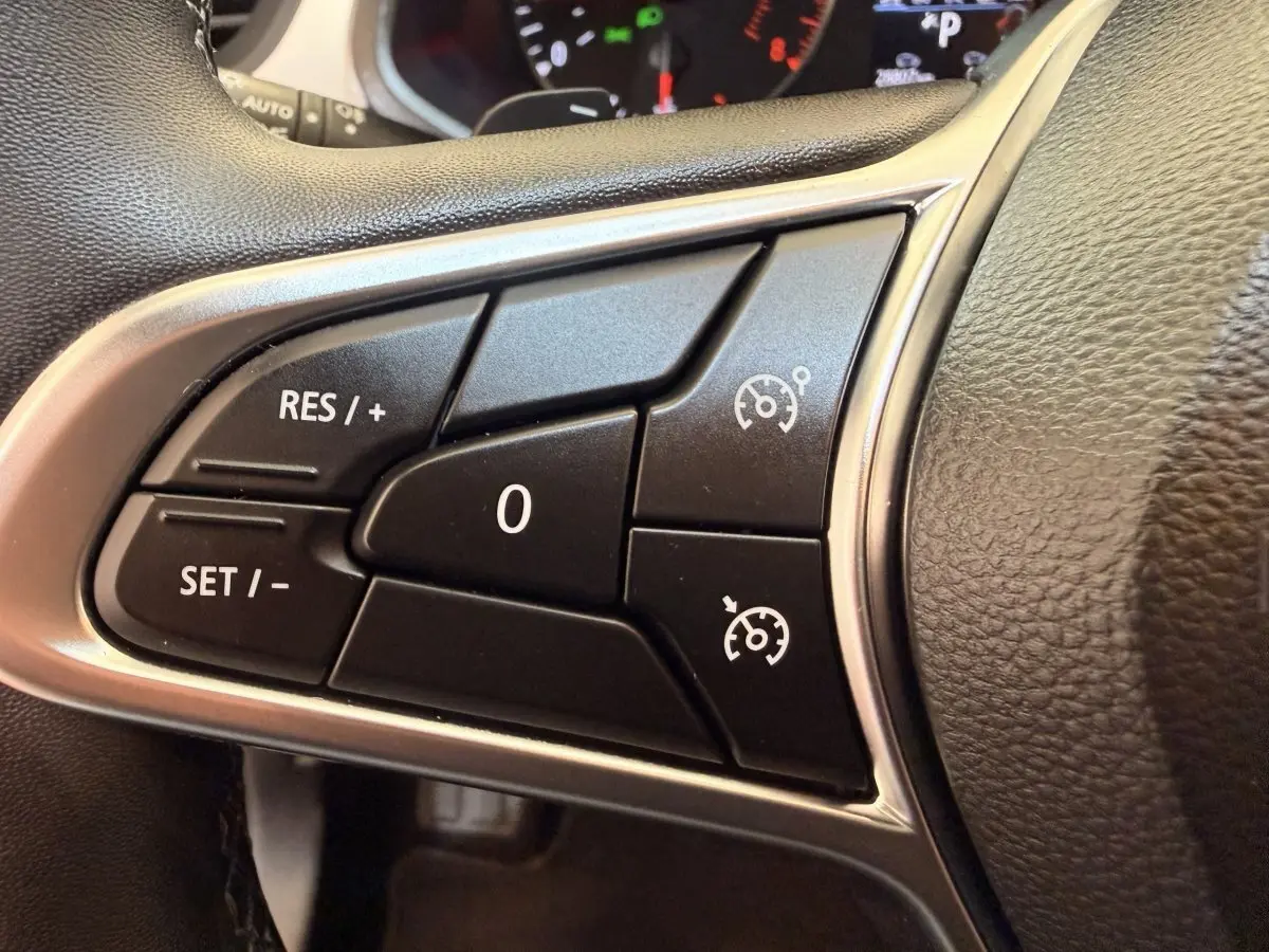 Gros plan sur les commandes de régulateur de vitesse à gauche du volant en cuir noir du Renault Captur blanc 2021.
