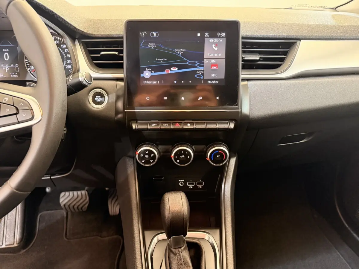 Vue intérieure centrée sur la console centrale et écran tactile du Renault Captur blanc, avec commandes climatisation et levier de boîte auto.
