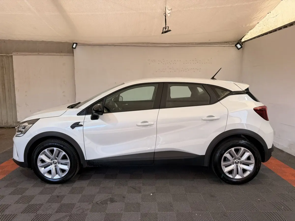 Profil côté gauche d’un Renault Captur blanc 2021 avec jantes alliage et rétroviseurs noirs dans un garage.