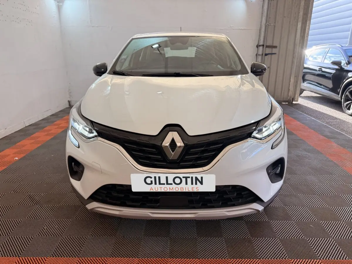 Vue avant d'un Renault Captur blanc 2021 dans un garage avec calandre noire et feux LED allumés.