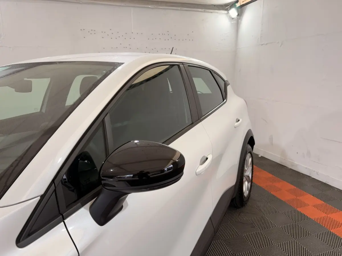 Vue de côté droit avant d’un Renault Captur blanc avec rétroviseur noir brillant dans un garage.