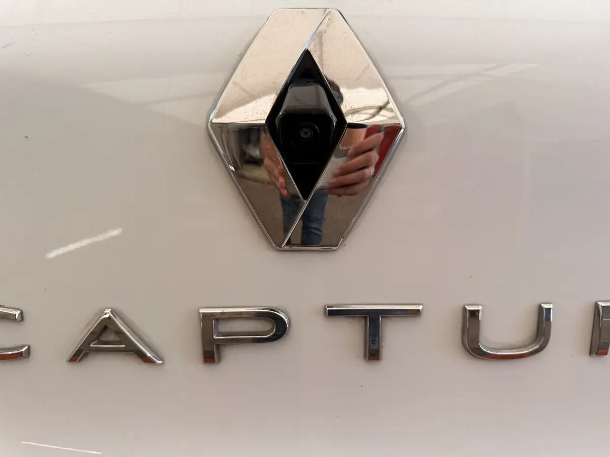 Gros plan sur le logo Renault avec caméra intégrée et lettrage CAPTUR sur la carrosserie blanche du véhicule.