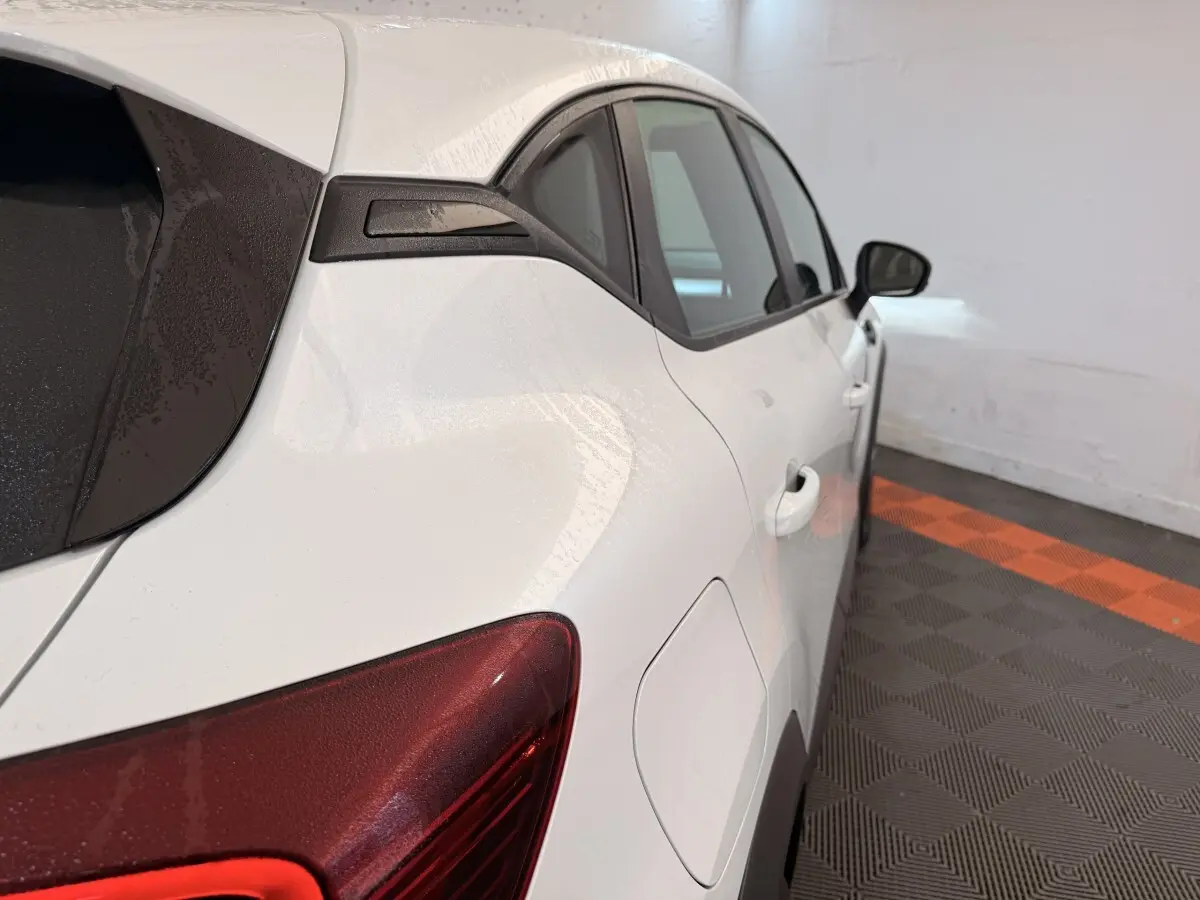 Vue arrière côté droit d’un Renault Captur blanc avec feux arrière rouges et vitres teintées dans un garage.