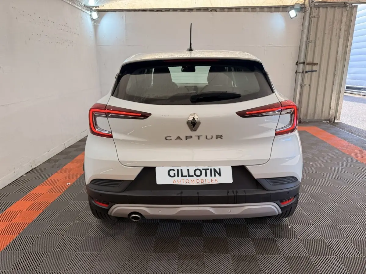 Vue arrière d’un Renault Captur blanc 2021 avec feux LED et logo central dans un garage éclairé.