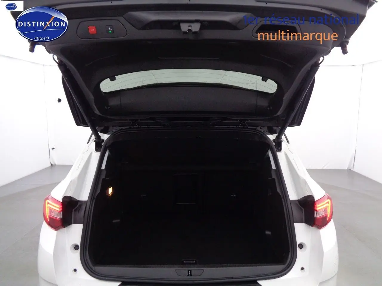 Vue arrière d'un Opel Grandland X blanc nacré avec hayon ouvert dévoilant un coffre spacieux et éclairé.