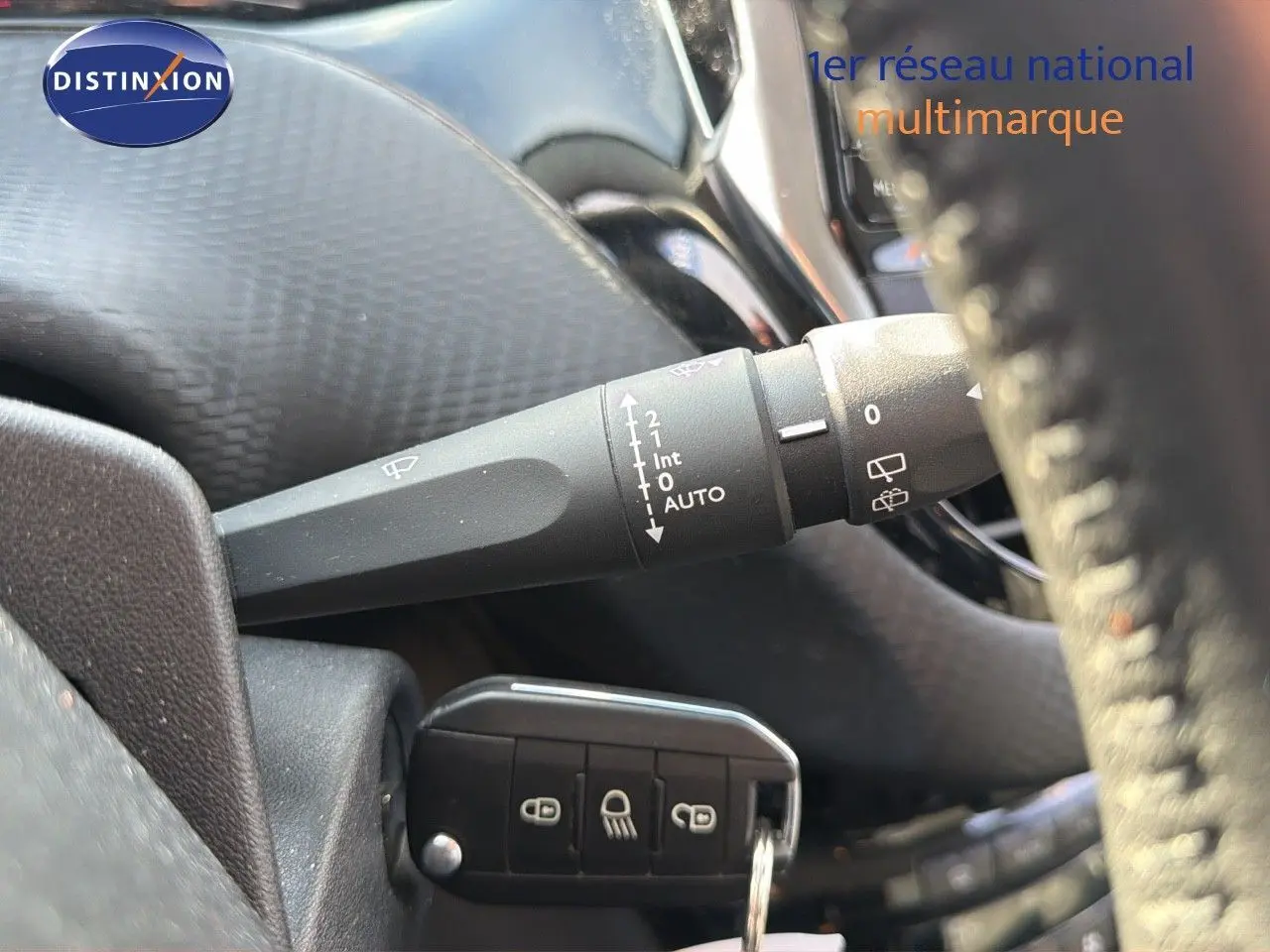 Gros plan sur la commande d'essuie-glace et la clé de contact d'une Peugeot 2008 gris platinium, intérieur noir.