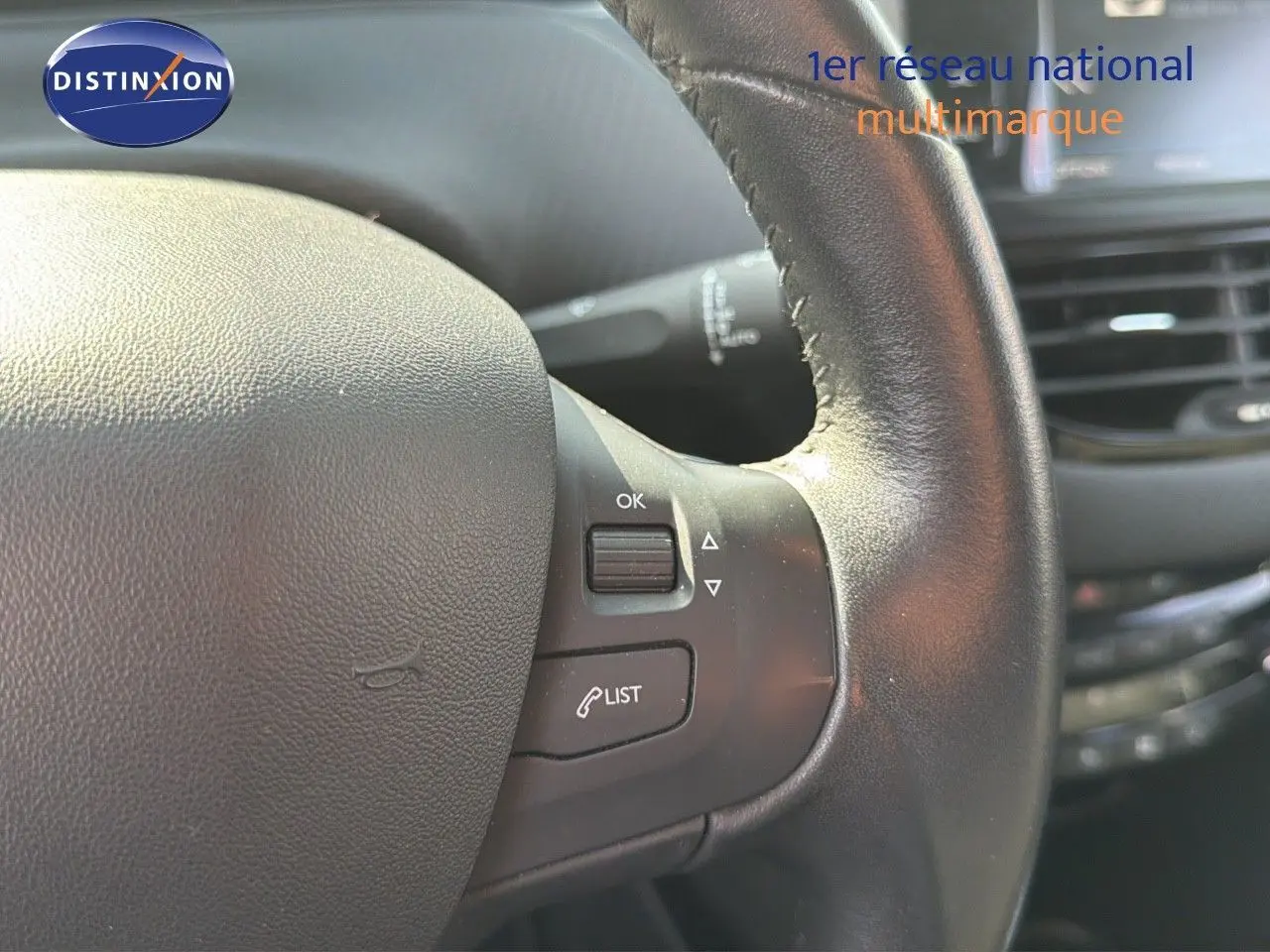 Gros plan sur le volant en cuir noir du Peugeot 2008 gris platinium, avec commandes intégrées et tableau de bord en arrière-plan.