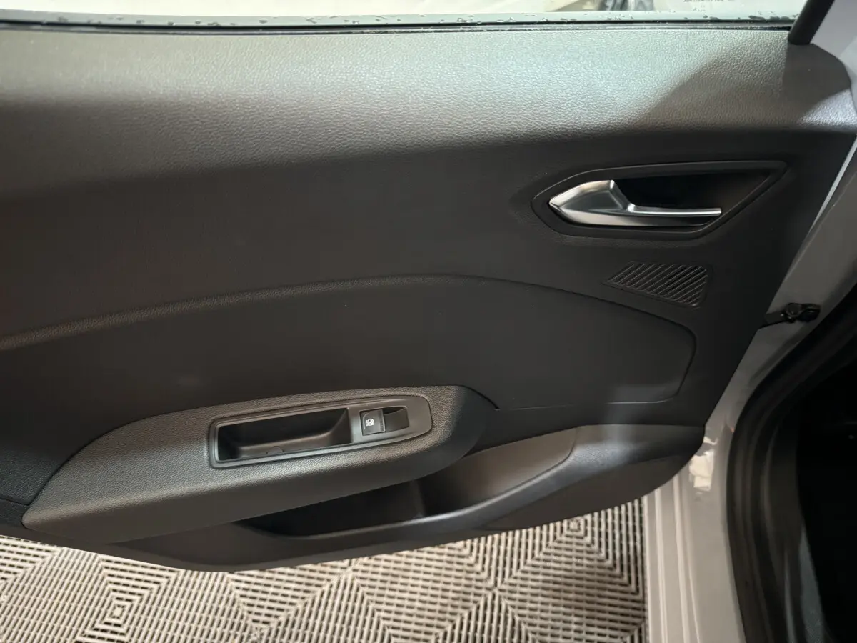 Gros plan sur la porte intérieure côté gauche d'une Renault Clio gris clair, avec poignée argentée et commande de vitre.