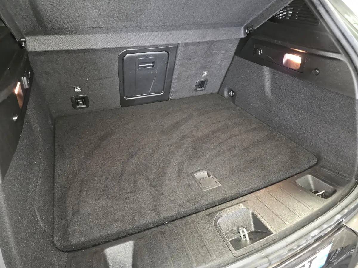 Coffre ouvert de l'Alfa Romeo Tonale gris, vue plongeante sur le tapis de sol et les rangements latéraux.