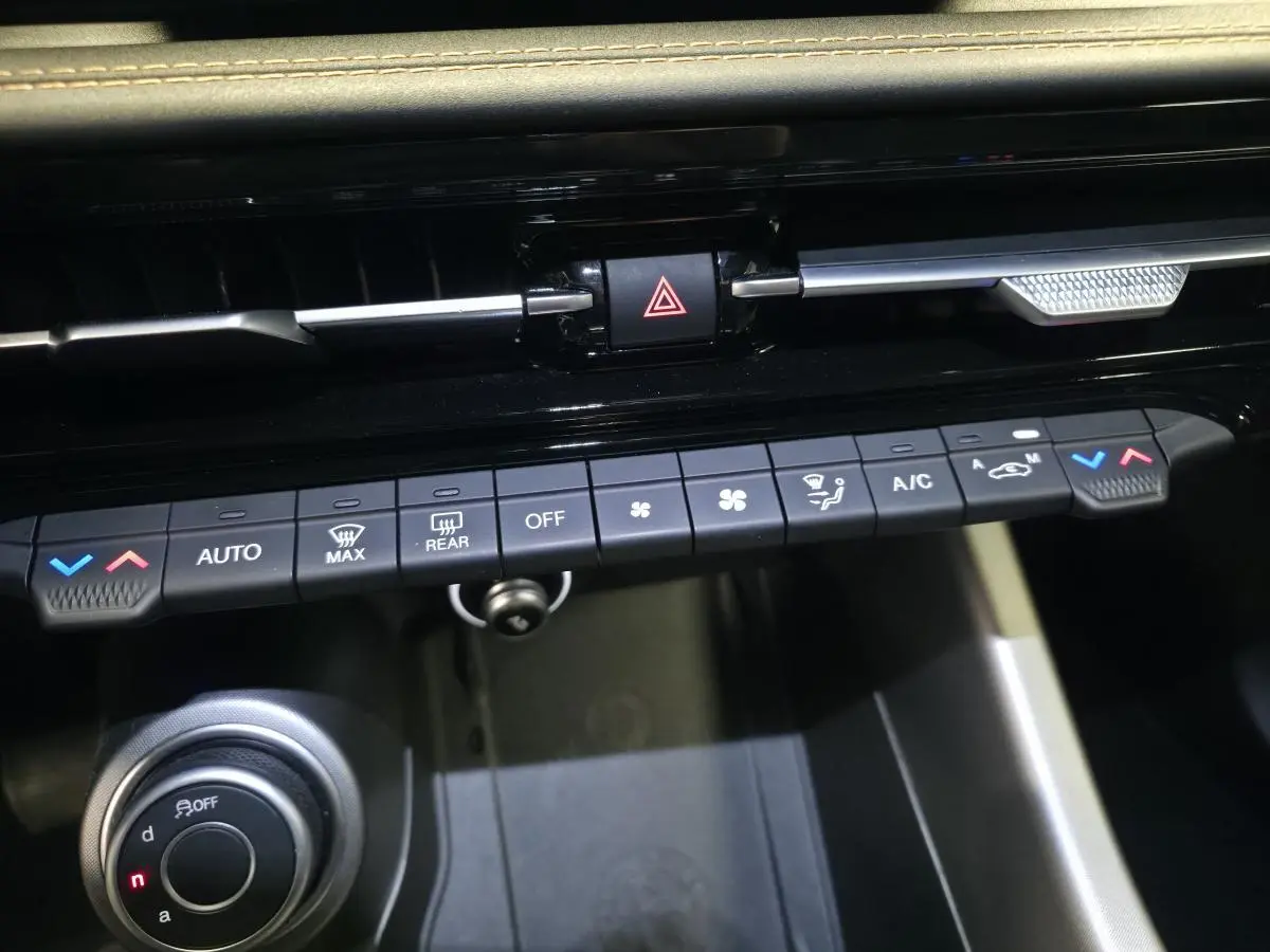 Vue rapprochée de la console centrale de l'Alfa Romeo Tonale grise, montrant les commandes de climatisation et le bouton de sélection de mode de conduite.