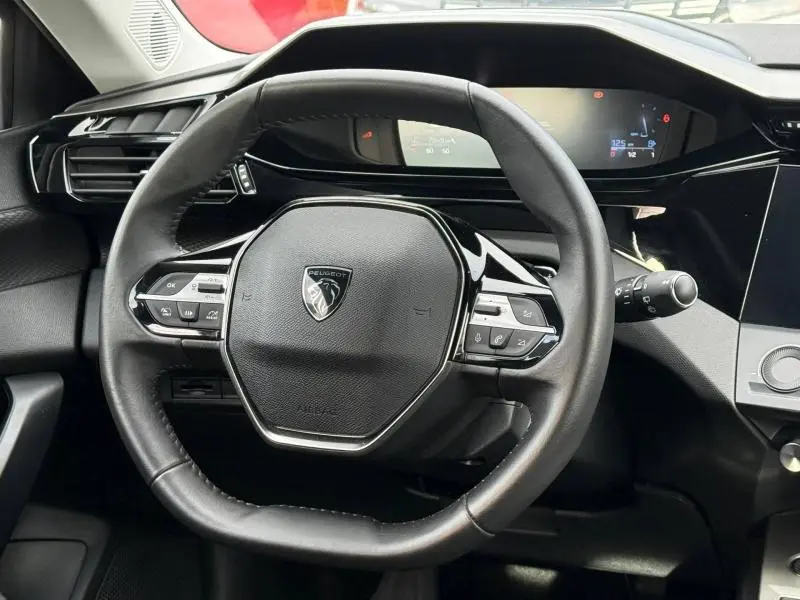 Vue rapprochée du volant noir de la Peugeot 308 2024 avec commandes intégrées et tableau de bord numérique en arrière-plan.