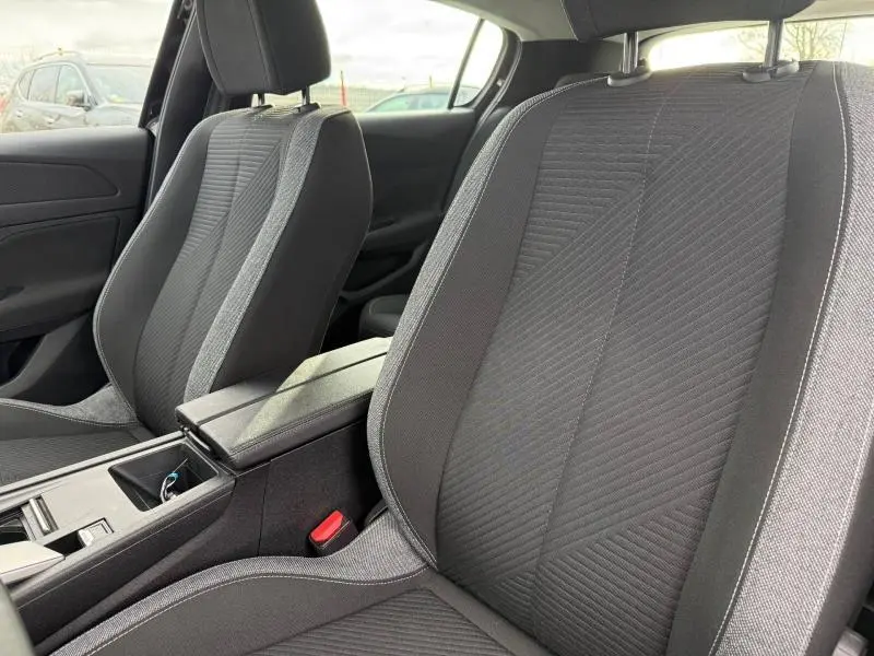 Vue intérieure rapprochée des sièges avant en tissu gris de la Peugeot 308 2024, avec accoudoir central et console.