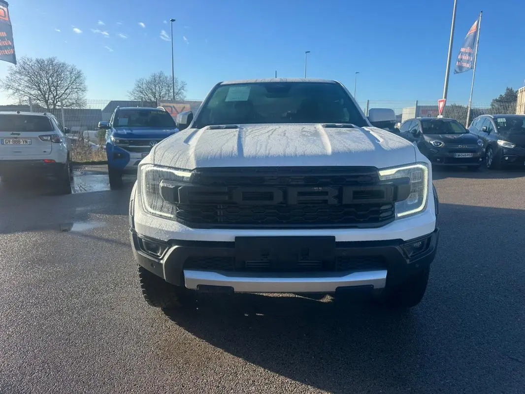 Ford Ranger Raptor blanc vu de face, calandre noire avec logo FORD en relief, phares LED allumés.