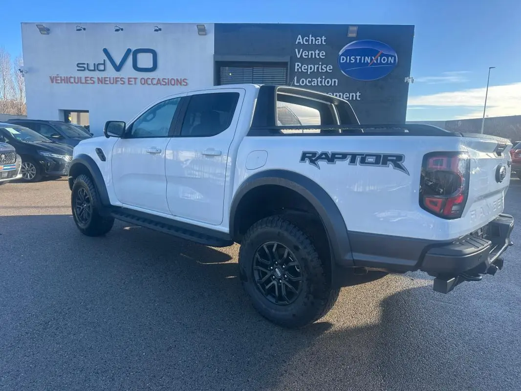 Ford Ranger Raptor blanc en 3/4 arrière droit, avec jantes alliage noires et logo Raptor visible sur la caisse.