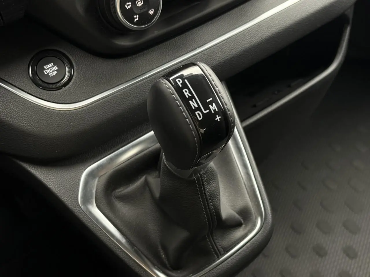 Gros plan sur le levier de vitesses automatique noir du Nissan Primastar gris, avec bouton start engine stop visible.