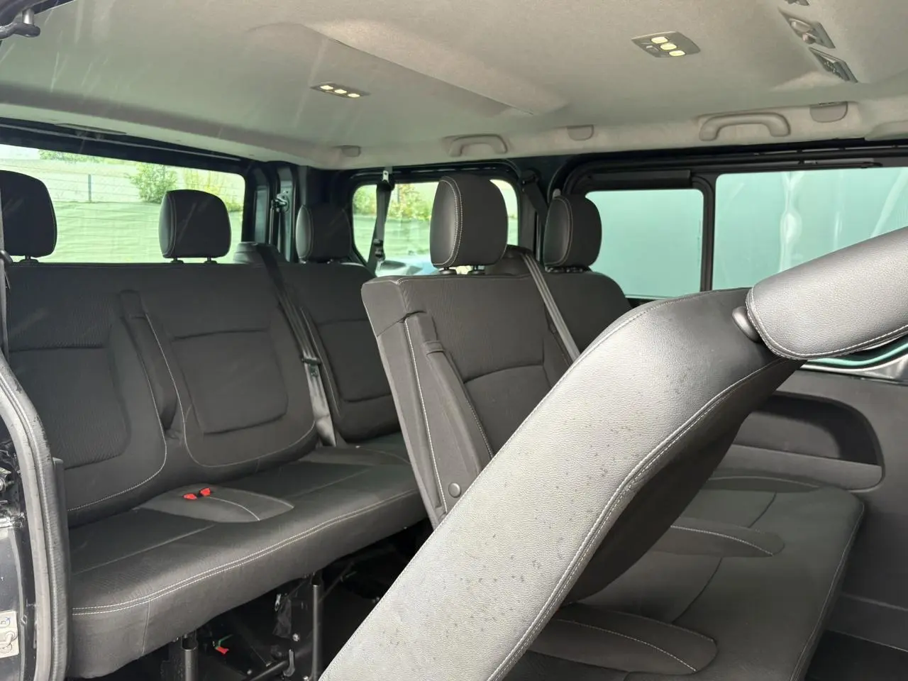 Vue intérieure côté droit du Nissan Primastar gris Comète montrant les sièges amovibles en tissu noir sur trois rangées.