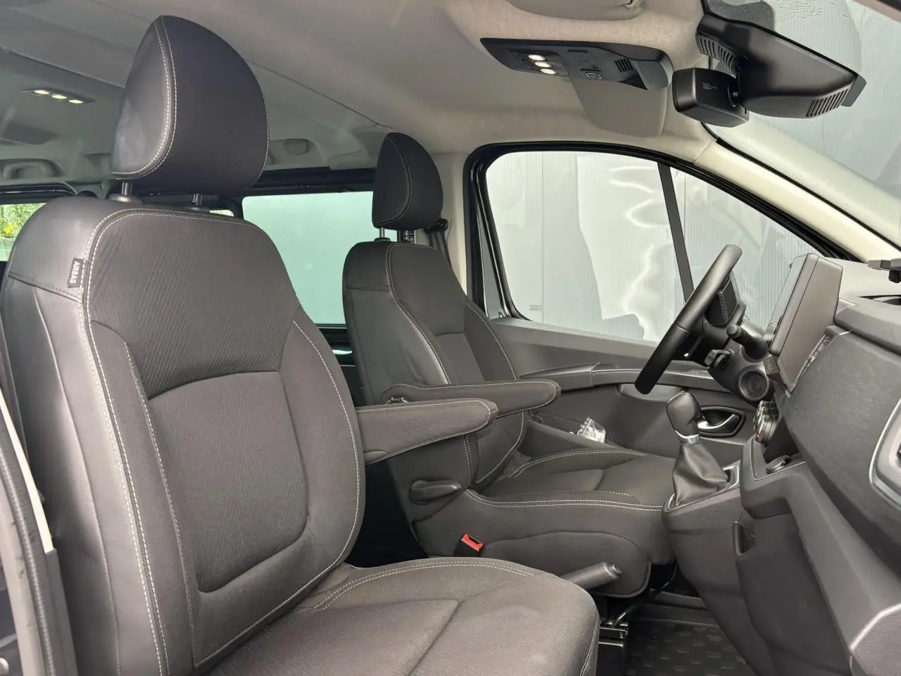 Vue intérieure côté conducteur du Nissan Primastar 2025, sièges noirs avec accoudoirs et tableau de bord moderne.