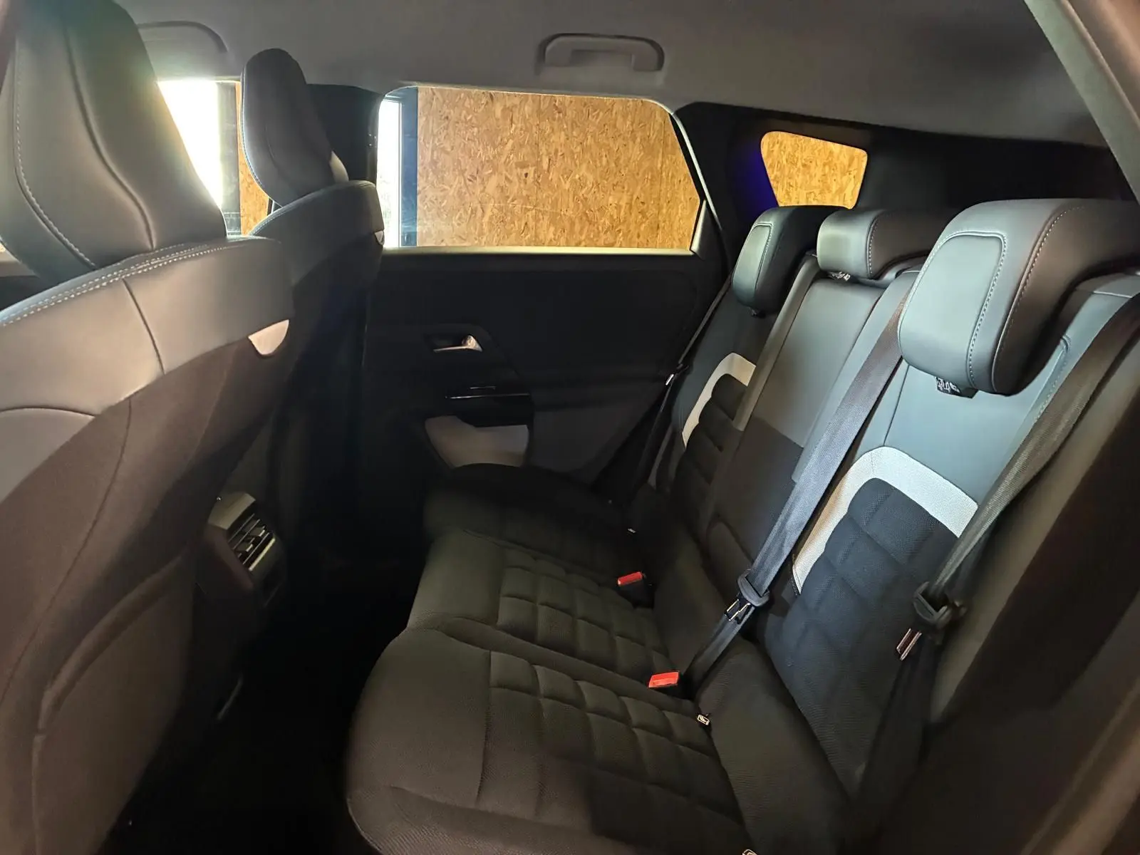 Vue intérieure arrière du Citroën C5 Aircross 1.2 hybride 2026, sièges tissu noir avec détails gris et ceintures visibles.