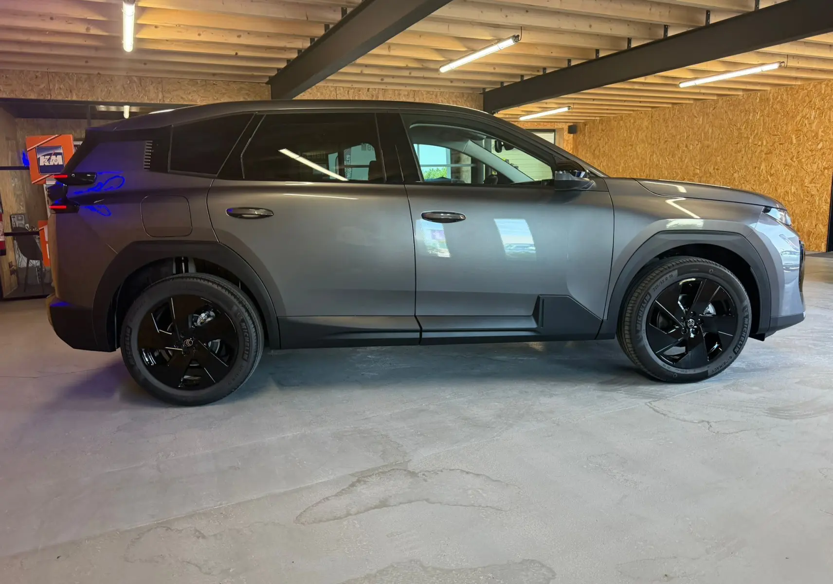 Vue de profil côté gauche d'un Citroën C5 Aircross gris 2026 avec jantes noires dans un garage en bois.