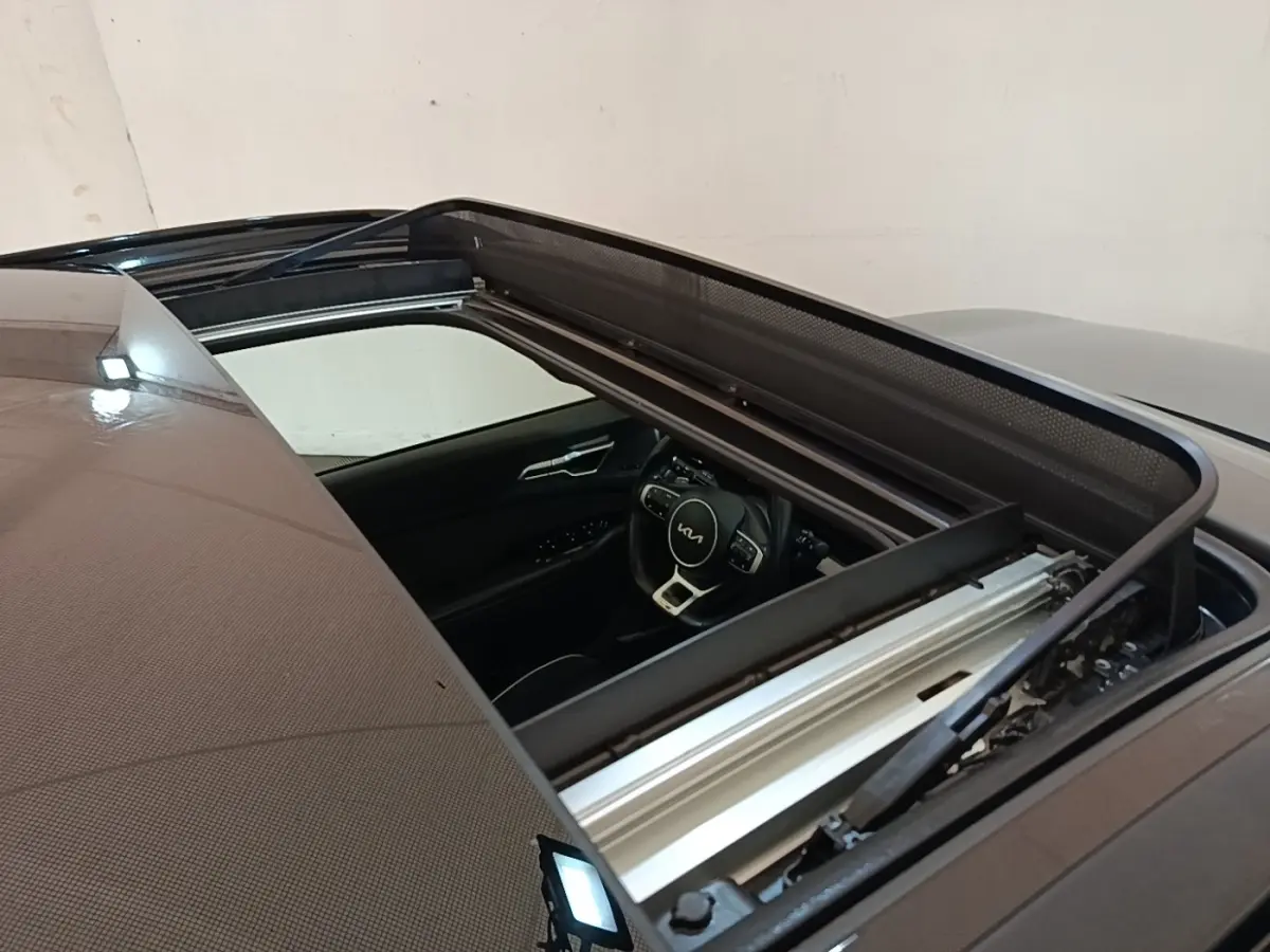 Vue plongeante sur le toit ouvrant ouvert d’un Kia Sportage gris clair, avec aperçu du volant et intérieur noir.