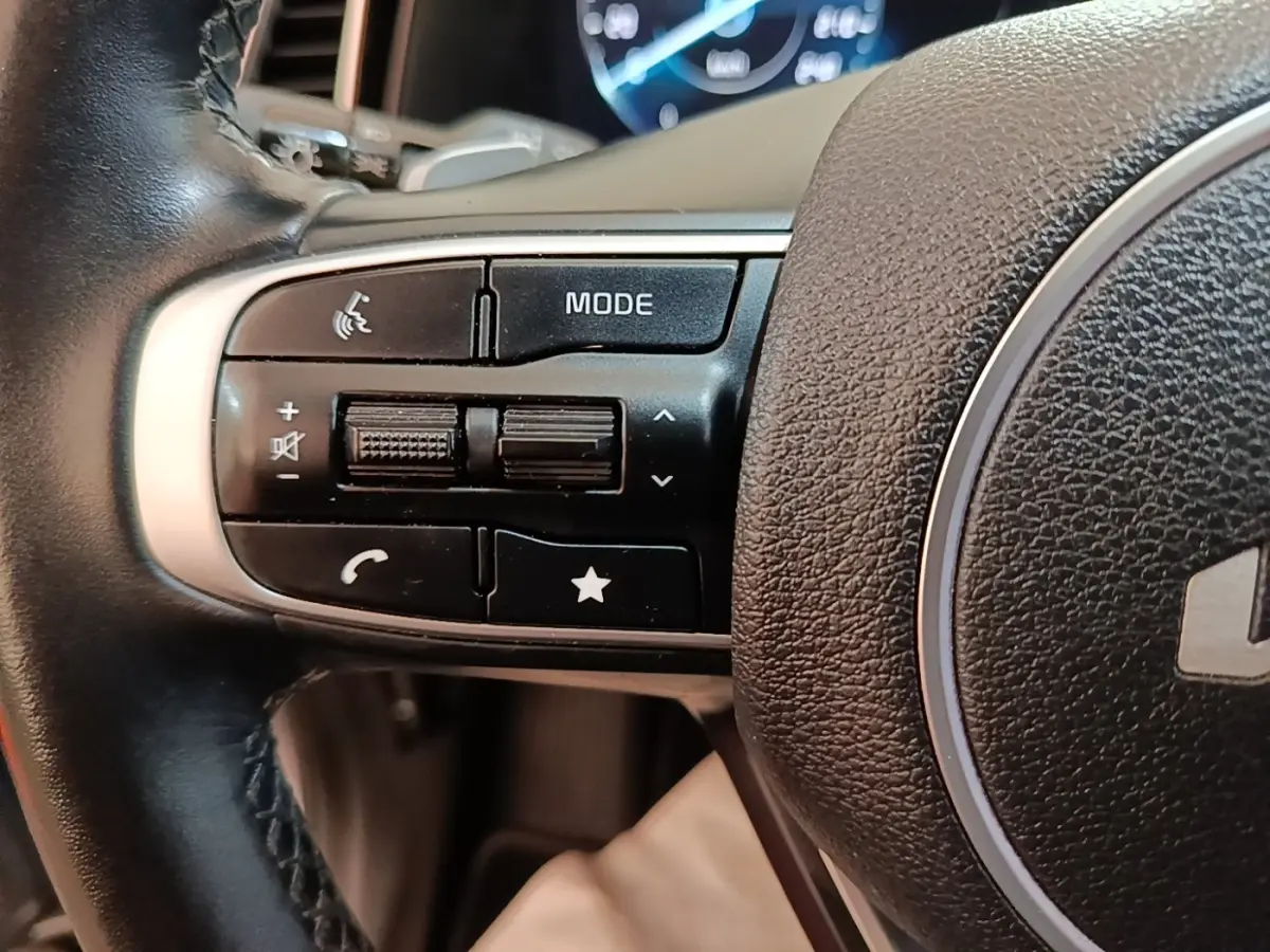 Gros plan sur les commandes gauche du volant cuir du Kia Sportage gris clair 2022 avec affichage numérique en arrière-plan.