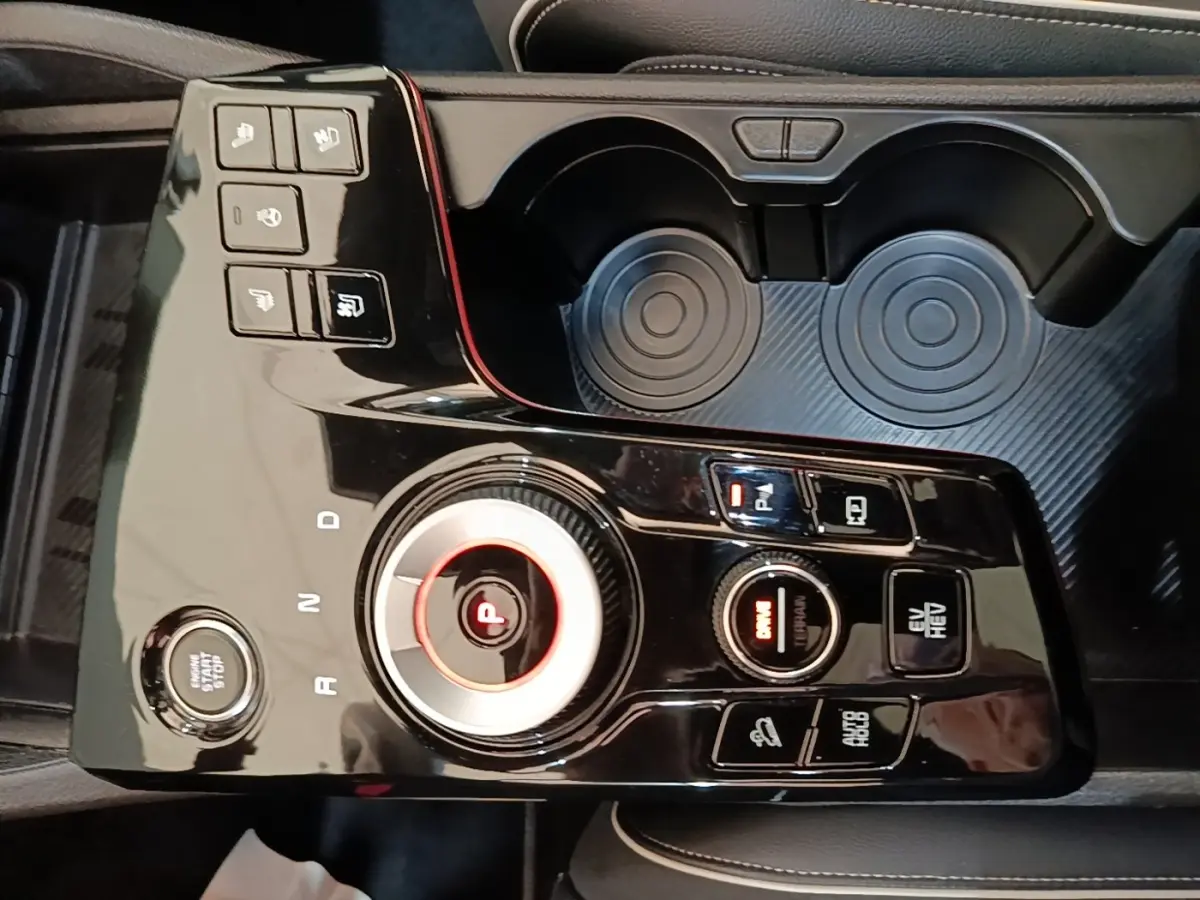Vue plongeante sur la console centrale noire brillante du Kia Sportage hybride rechargeable avec molette de sélection de vitesse et boutons multifonctions.