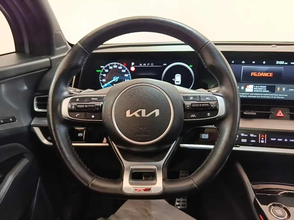 Vue intérieure centrée sur le volant cuir noir du Kia Sportage gris clair avec tableau de bord digital et écran tactile.