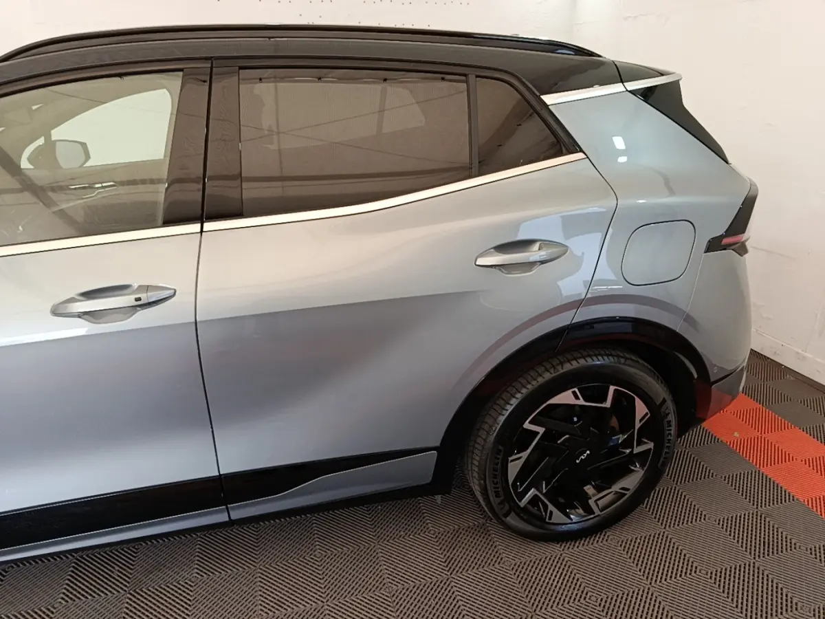 Vue latérale droite du Kia Sportage gris clair hybride rechargeable, mettant en valeur la porte arrière et la roue au design moderne.