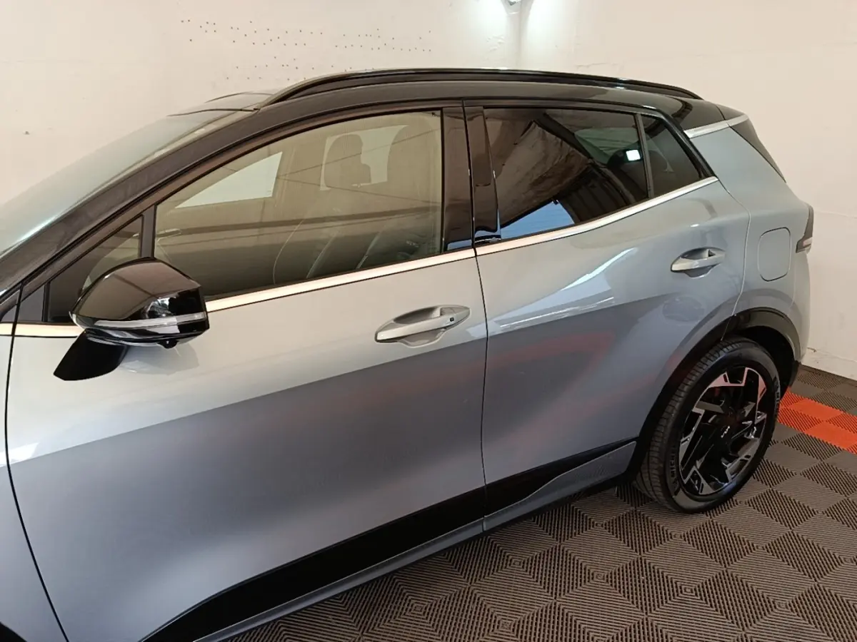 Vue latérale côté gauche d'un KIA Sportage gris clair avec toit noir et jantes noires design.