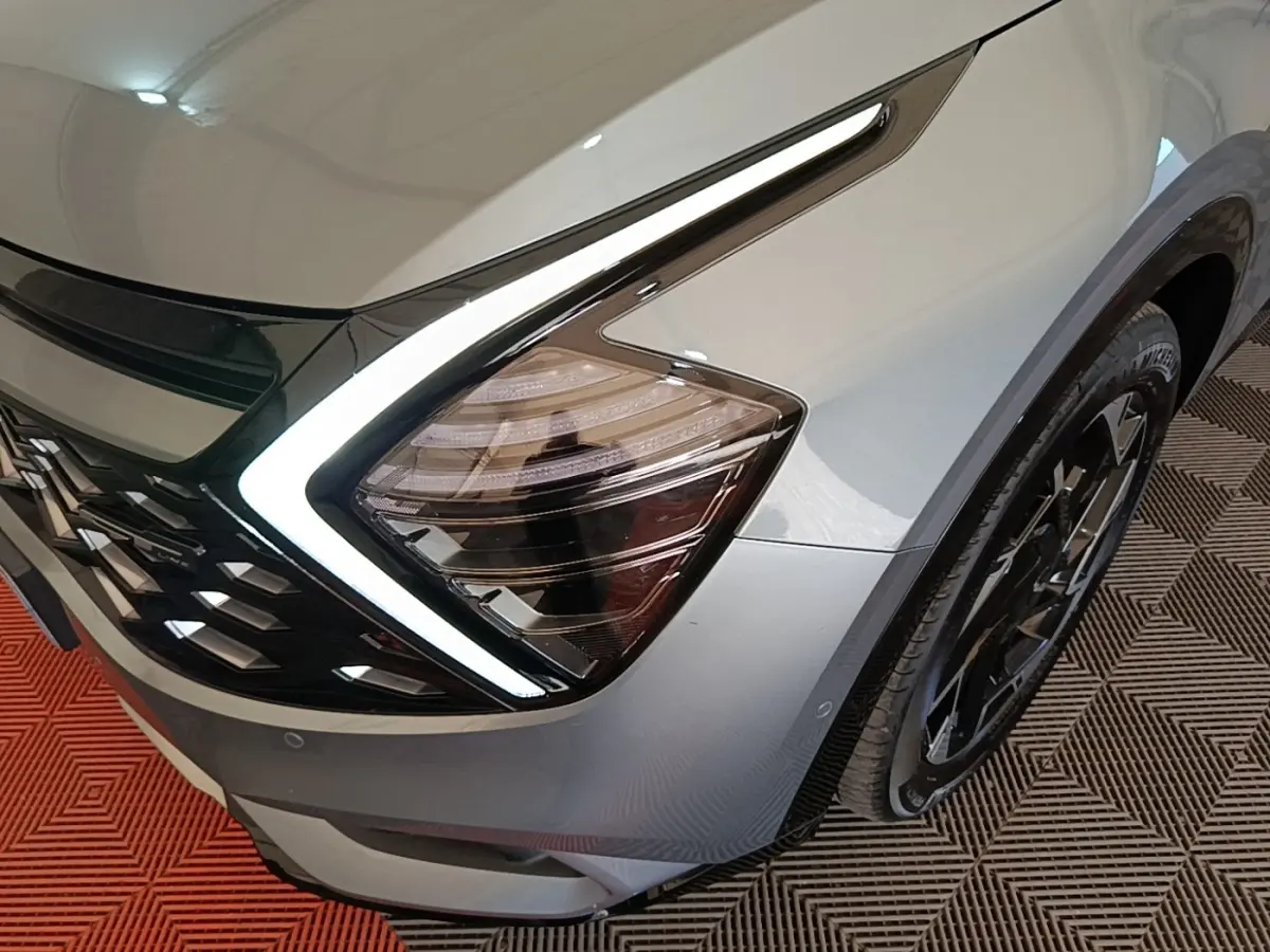 Gros plan sur l'avant droit gris clair du KIA SPORTAGE 2022 avec phare LED en forme de boomerang et jante noire.