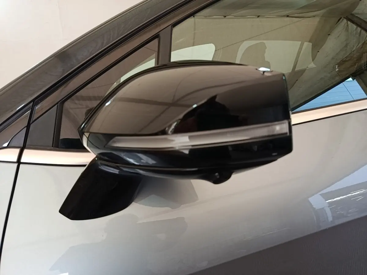 Rétroviseur noir en gros plan côté gauche d’un KIA SPORTAGE gris clair avec fenêtre arrière visible en arrière-plan.