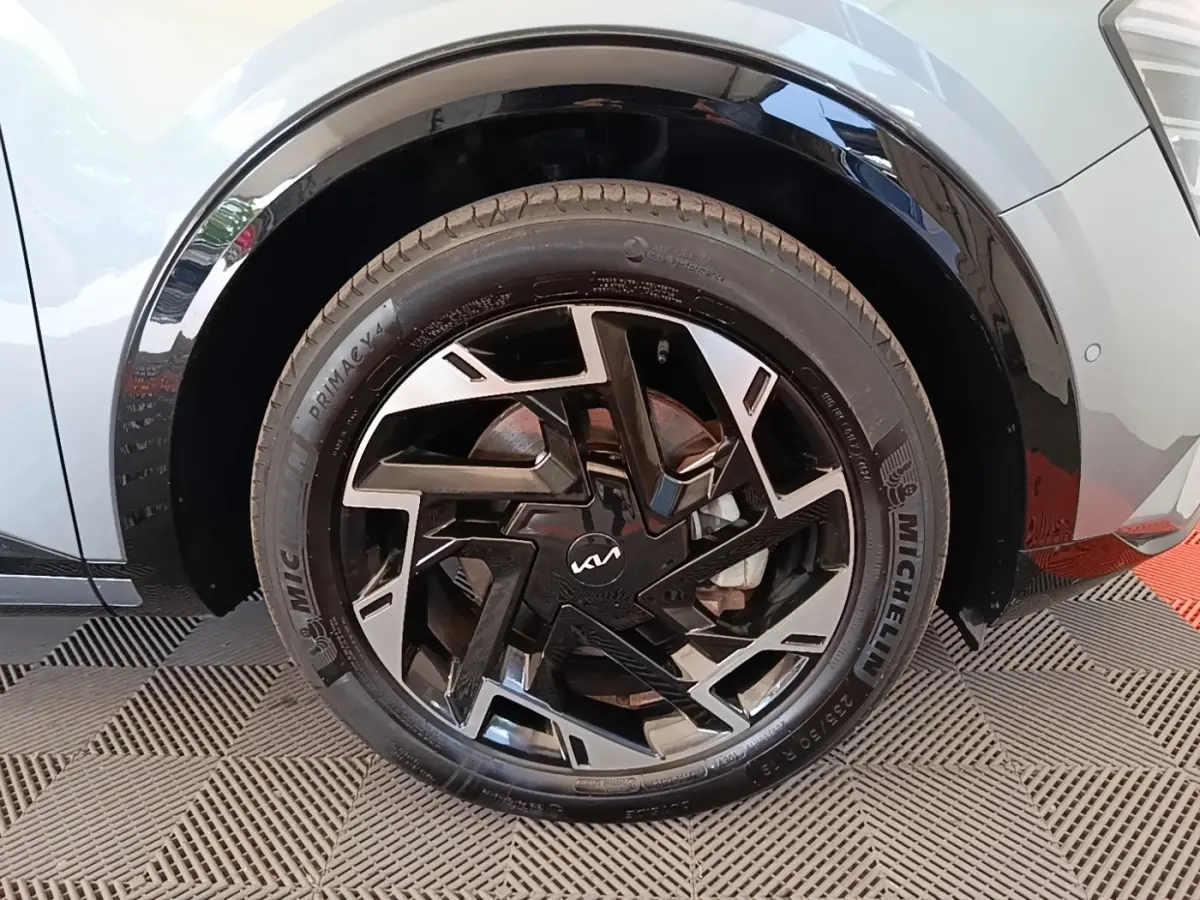 Gros plan sur la roue avant gauche du KIA Sportage gris clair, mettant en valeur la jante noire et argentée au design géométrique.