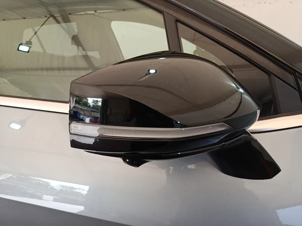 Rétroviseur noir côté gauche d’un KIA Sportage gris clair 2022 avec clignotant intégré, vue rapprochée.