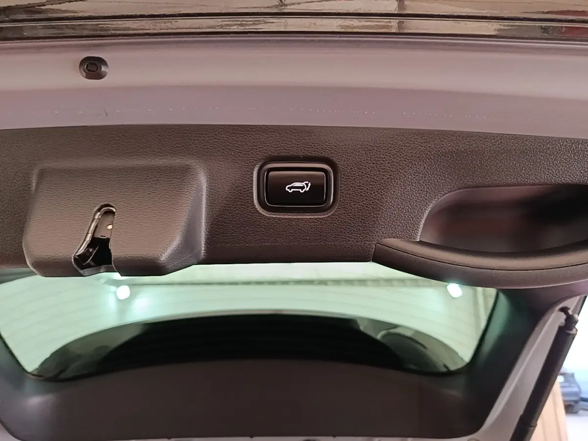 Bouton d'ouverture électrique du coffre sur la partie intérieure du hayon d'un KIA Sportage gris clair.