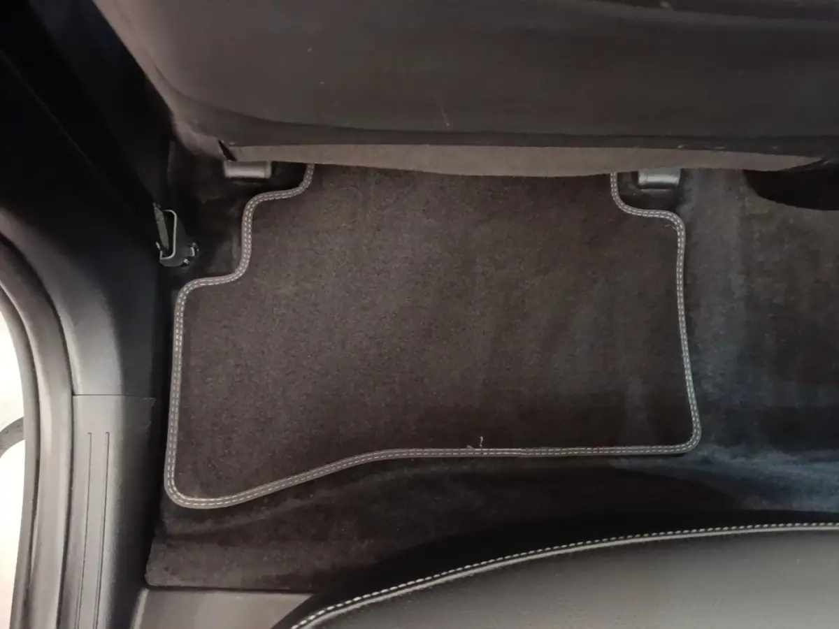 Détail du tapis de sol noir avec surpiqûres blanches sous le siège arrière du Kia Sportage gris clair 2022 hybride rechargeable.