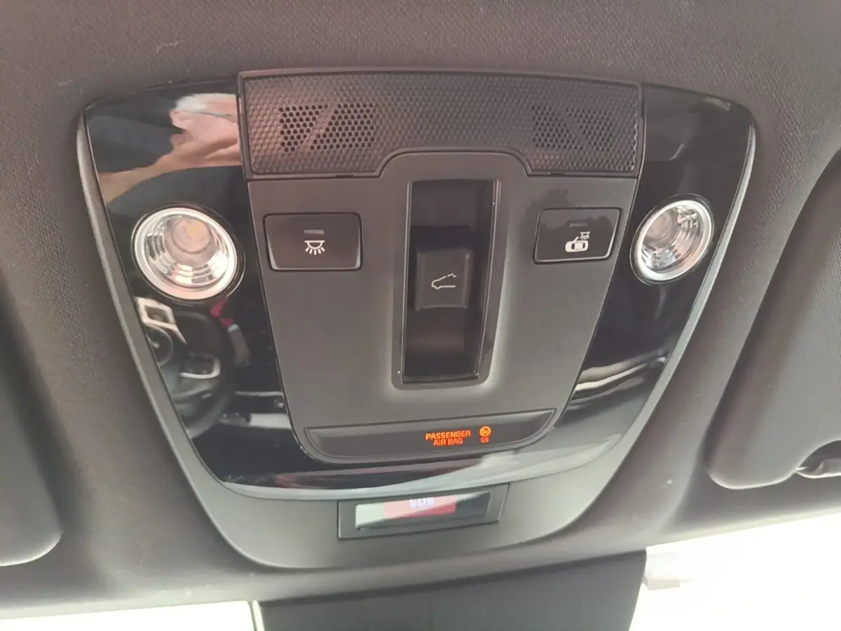 Vue rapprochée du panneau de commande de toit noir brillant avec éclairage et indicateur airbag passager actif dans un Kia Sportage gris clair 2022.