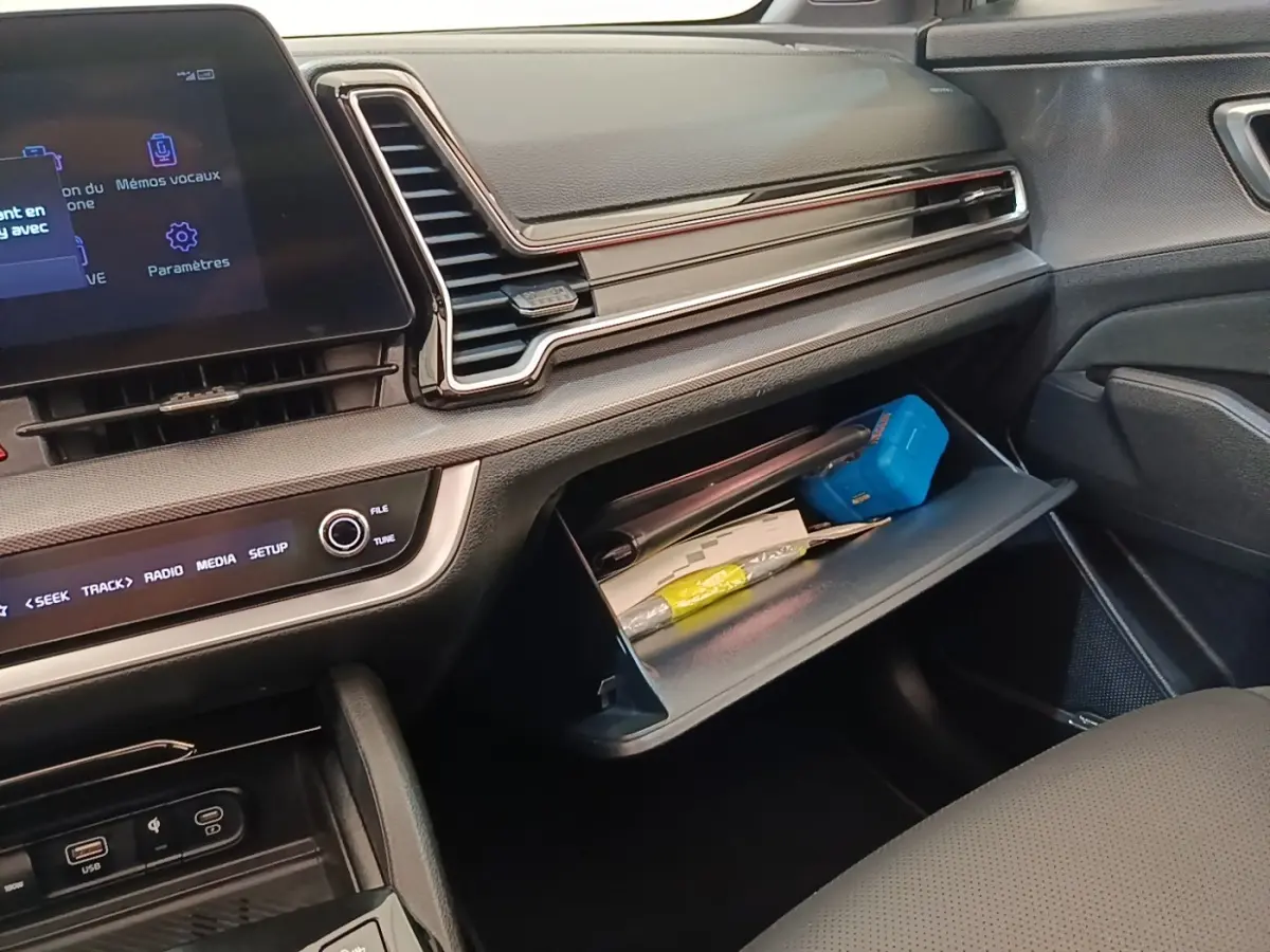 Intérieur du Kia Sportage 2022, vue côté passager sur la boîte à gants ouverte et tableau de bord moderne noir.