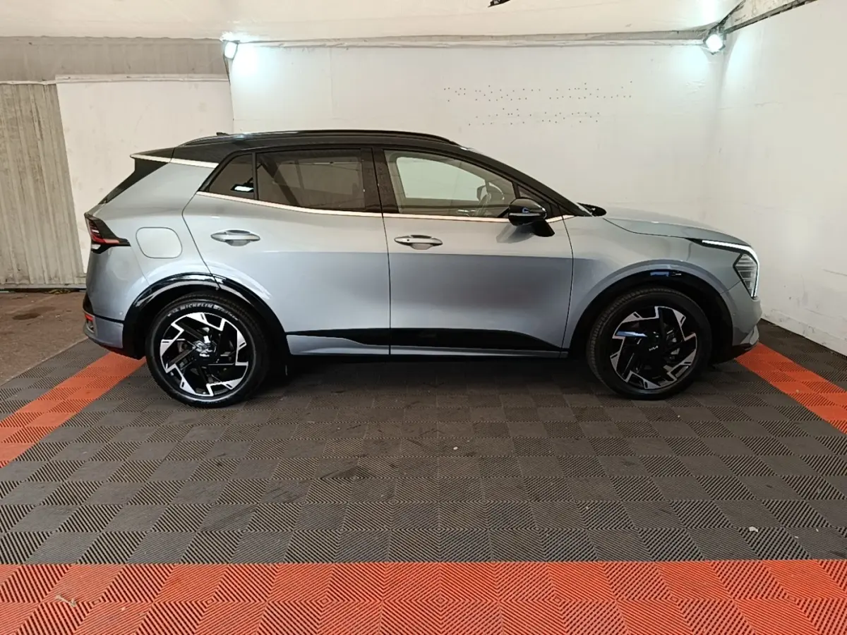 Vue de profil côté gauche d'un KIA Sportage gris clair avec toit noir et jantes noires design moderne dans un garage.