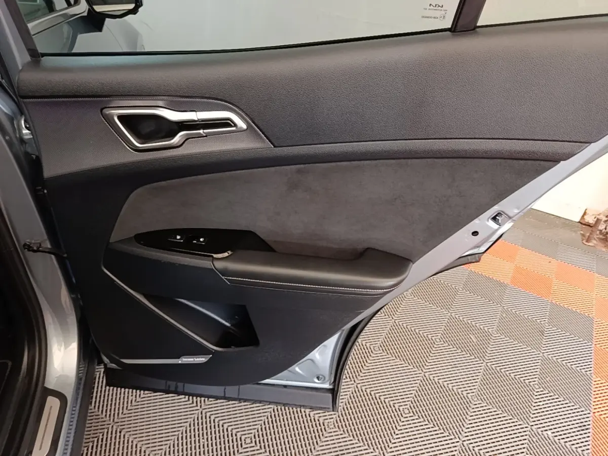 Vue intérieure côté gauche de la porte arrière grise claire du Kia Sportage avec garniture noire et commandes de fenêtre.