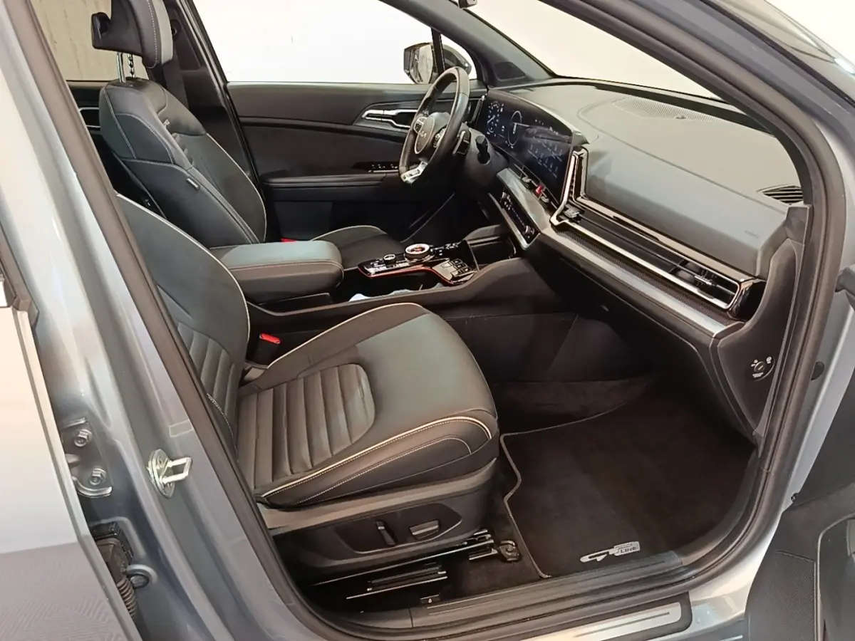 Intérieur avant droit du KIA Sportage gris clair 2022, sièges cuir noirs et tableau de bord digital large.
