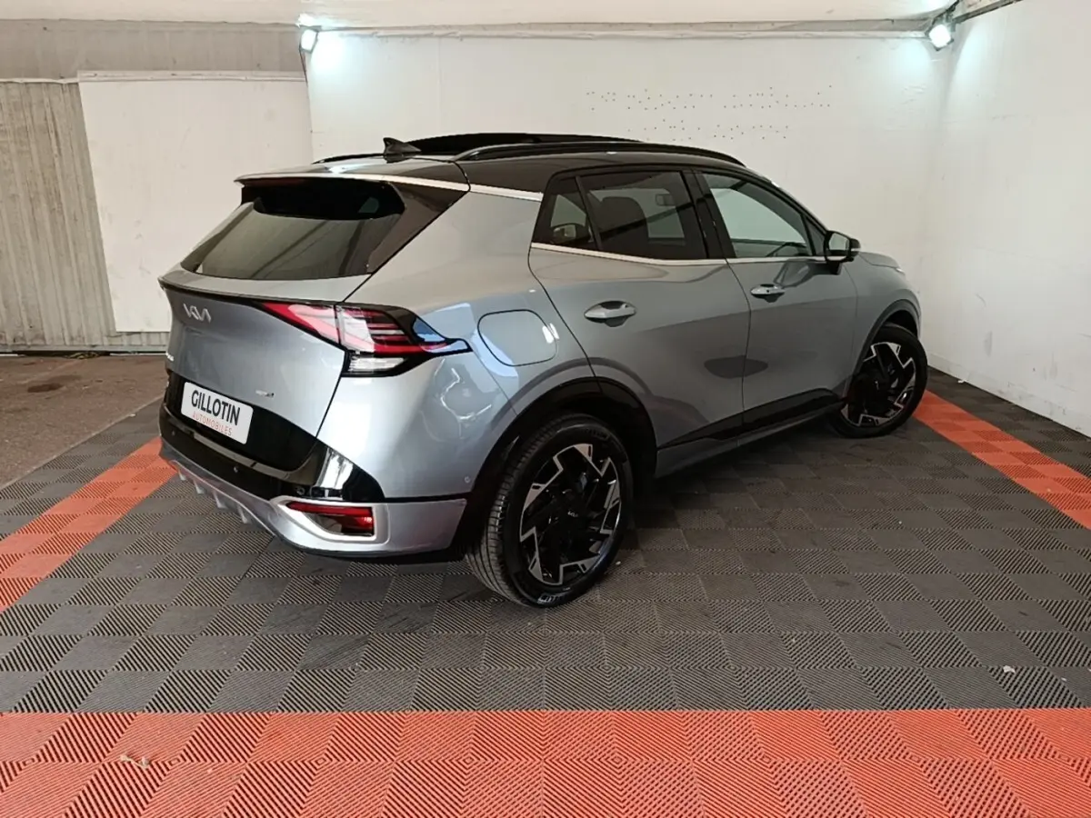 Vue 3/4 arrière droite d'un KIA SPORTAGE gris clair avec toit noir et jantes noires au design moderne.