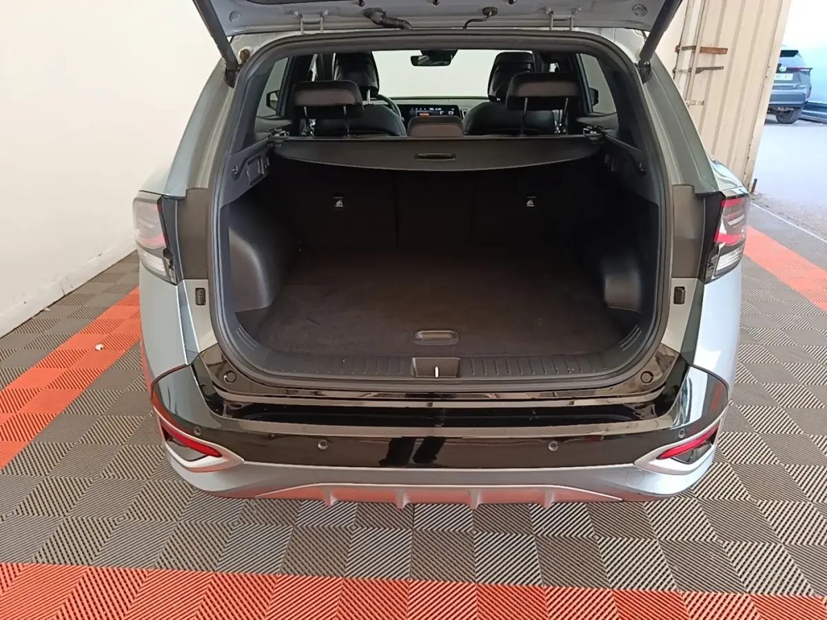 Vue arrière ouverte du Kia Sportage gris clair 2022 montrant le coffre spacieux et la finition noire brillante du pare-chocs.
