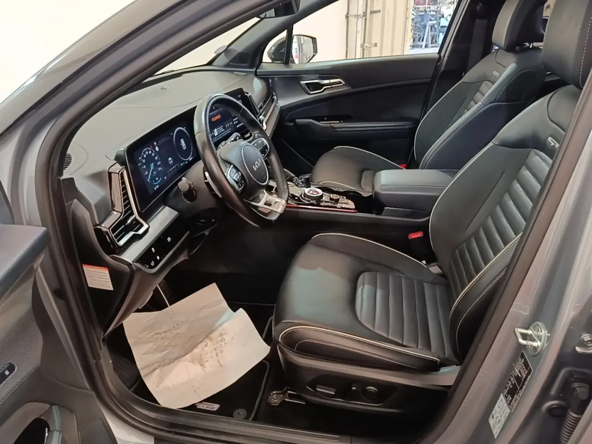 Vue intérieure côté conducteur du Kia Sportage 2022 avec sièges cuir noirs et tableau de bord digital lumineux.