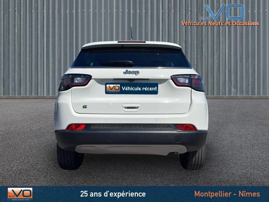 Vue arrière d'un Jeep Compass blanc 2024 avec feux arrière fumés et logo Jeep visible sur fond urbain.