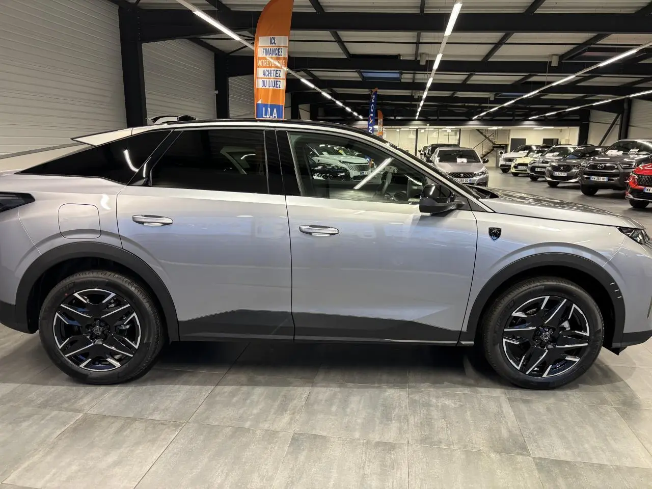 Vue de profil côté gauche d’un Peugeot 3008 gris Artense avec jantes alliage noires et toit noir en showroom.