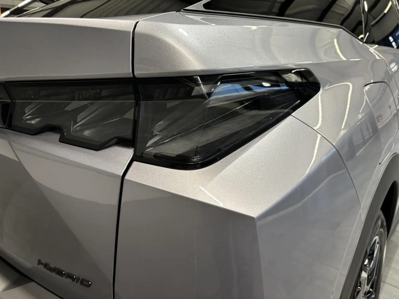Gros plan sur le feu arrière droit et la carrosserie gris Artense du Peugeot 3008 Hybrid 2025, avec détails anguleux.