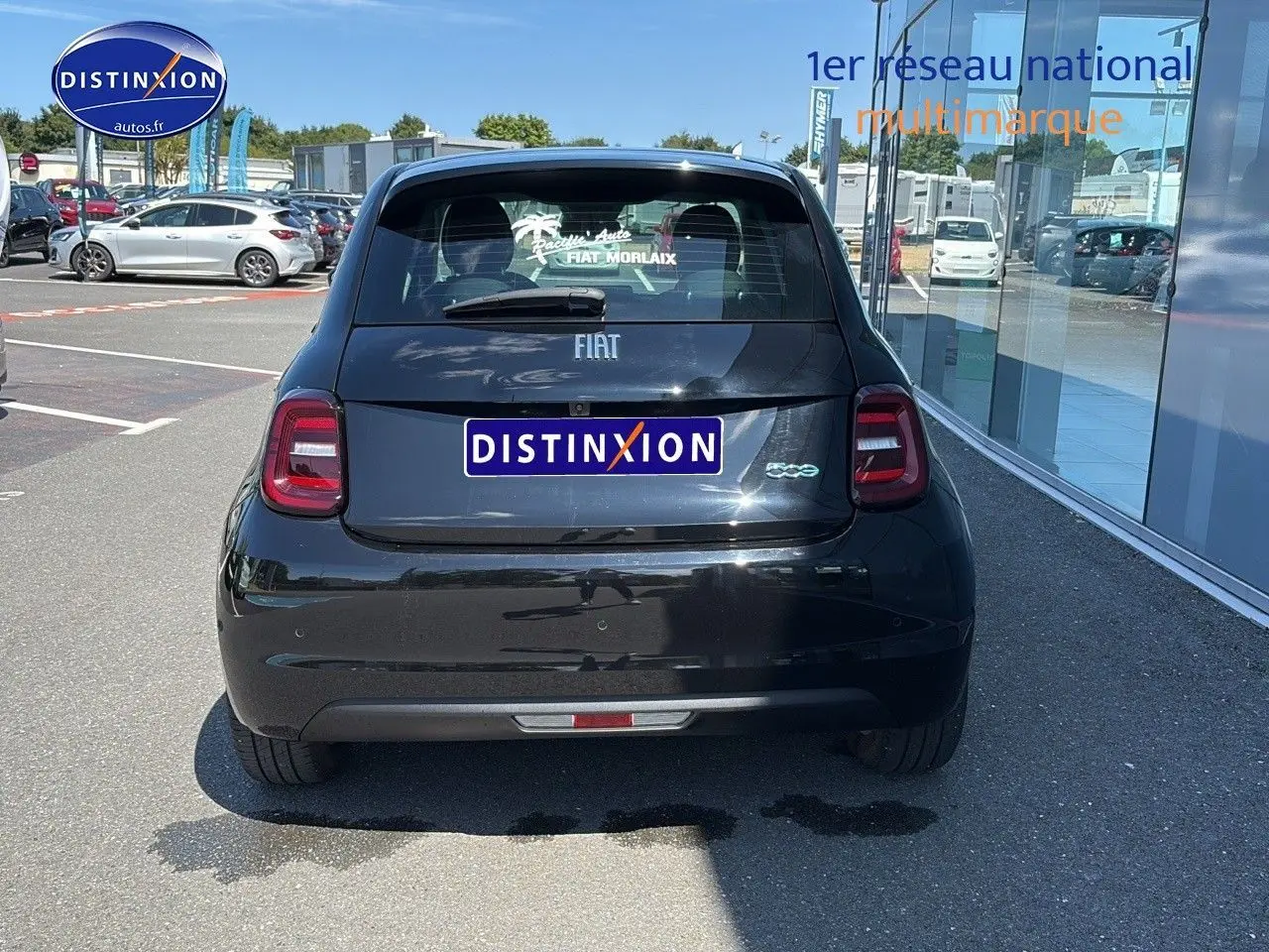 Vue arrière d'une Fiat 500 électrique noire stationnée devant une vitrine avec logo Distinxion sur la plaque.
